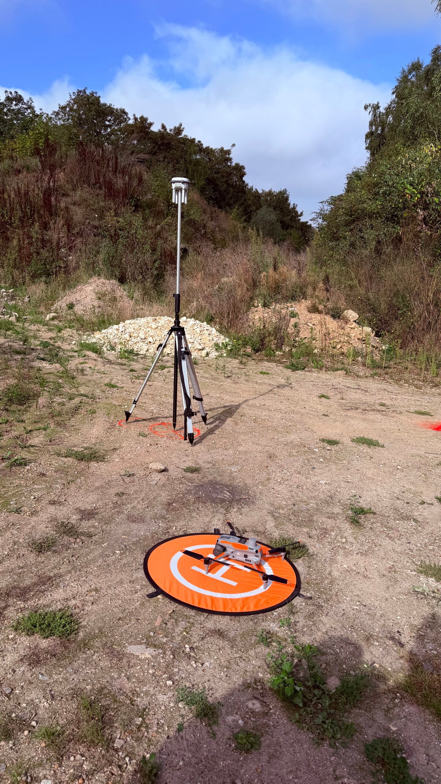 Drone DJI Matrice 4E posé sur une piste de décollage et station GNSS D-RTK 3 montée sur trépied